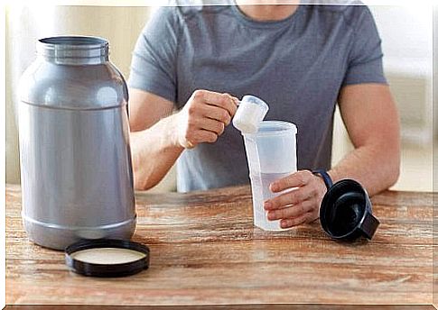 A man sits at the table and pours some powdered creatine into his drink.